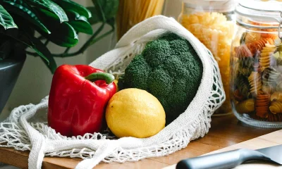Brokkoli, Paprika und Zitrone in Einkaufsnetz vor mit Nudeln gefüllten Gläsern