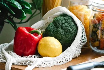 Brokkoli, Paprika und Zitrone in Einkaufsnetz vor mit Nudeln gefüllten Gläsern