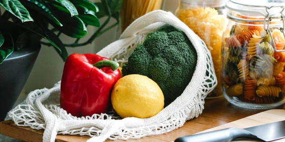 Brokkoli, Paprika und Zitrone in Einkaufsnetz vor mit Nudeln gefüllten Gläsern