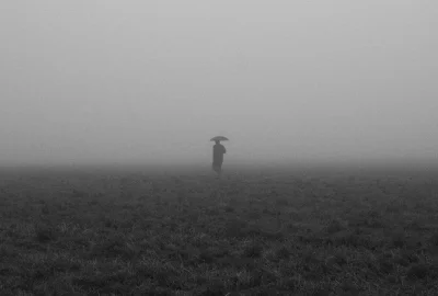 Person mit Regenschirm am Horizont auf nebliger Ebene