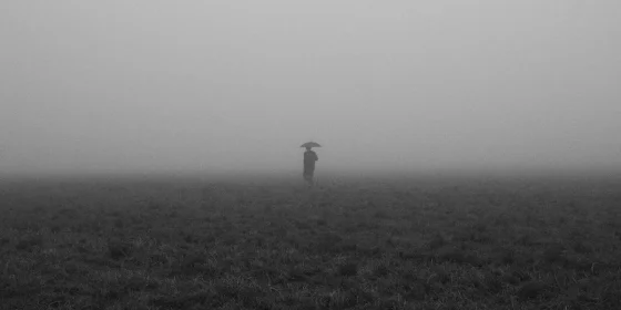 Person mit Regenschirm am Horizont auf nebliger Ebene