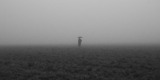 Person mit Regenschirm am Horizont auf nebliger Ebene