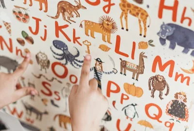 Kinderhände zeigen auf verschiedene Tiere auf einer Buchstabentafel