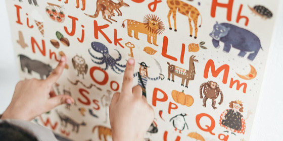 Kinderhände zeigen auf verschiedene Tiere auf einer Buchstabentafel