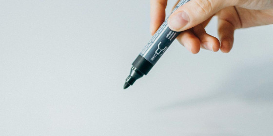 Eine Hand führt einen Filzstift auf ein leeres Blatt Papier