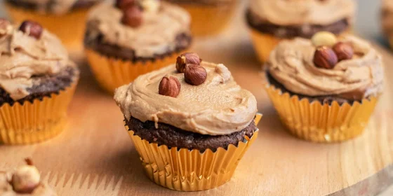 Mehrere Muffins auf einem Holzteller, garniert mit Creme und Haselnüssen