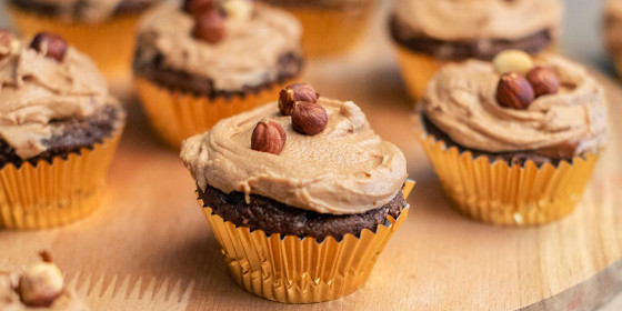 Mehrere Muffins auf einem Holzteller, garniert mit Creme und Haselnüssen