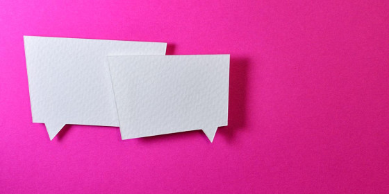 Zwei Sprechblasen aus Papier vor pinkfarbenem Hintergrund